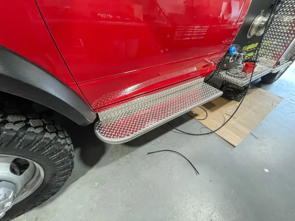 Exterior view of small fire truck showing cab, body compartments, and wheel/tire area.